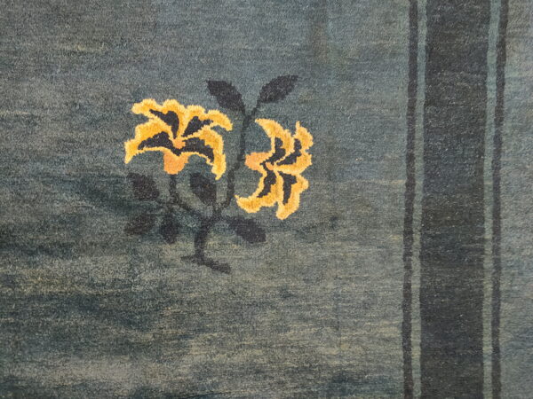 Low-pile teal rug detail showing yellow floral motifs, dark stems, and vertical navy stripes along the right edge.