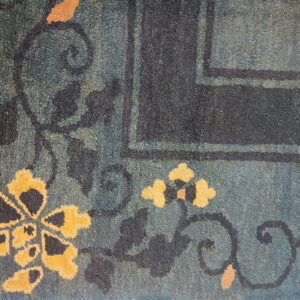 Textured blue-green rug detail with large yellow flowers, dark scrolling vines, and a navy border.