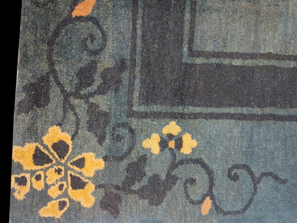 Textured blue-green rug detail with large yellow flowers, dark scrolling vines, and a navy border.