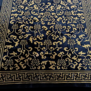 Navy and gold low-pile rug featuring a densely detailed floral pattern and thick geometric meander border.