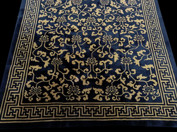 Navy and gold low-pile rug featuring a densely detailed floral pattern and thick geometric meander border.