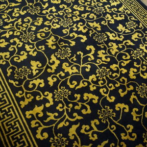 Black rug featuring a dense gold vine and floral pattern with a geometric border on wood flooring.
