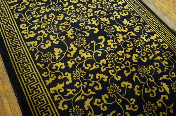 Black rug featuring a dense gold vine and floral pattern with a geometric border on wood flooring.
