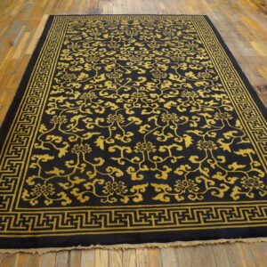 Black rug with gold scroll pattern and geometric border on distressed hardwood planks.