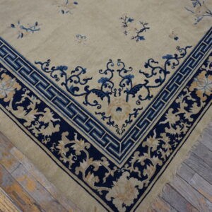 Low pile beige rug with navy blue and gold floral borders resting on distressed wooden planks.