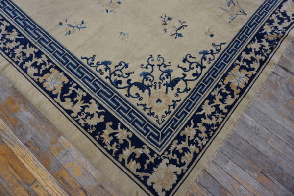 Low pile beige rug with navy blue and gold floral borders resting on distressed wooden planks.