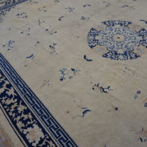 Low pile beige rug with a navy border featuring floral scrolls and a fret pattern on rustic wood flooring.
