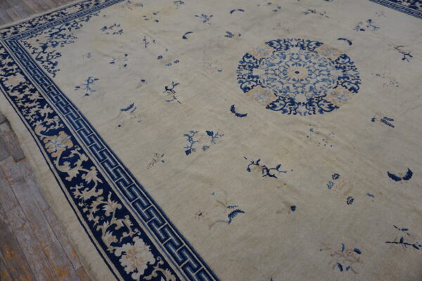 Low pile beige rug with a navy border featuring floral scrolls and a fret pattern on rustic wood flooring.