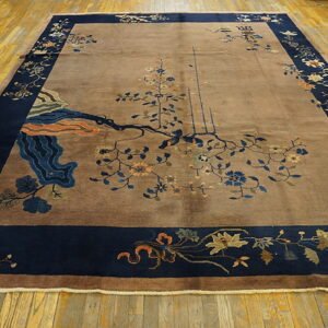 A plush tan rug with a wide navy blue floral border lies on light wooden floor planks.