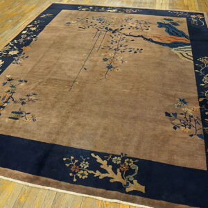 Brown high-pile rug with a navy blue floral border and asymmetrical tree designs laid on yellowish wooden floorboards.