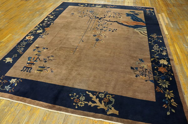 Brown high-pile rug with a navy blue floral border and asymmetrical tree designs laid on yellowish wooden floorboards.