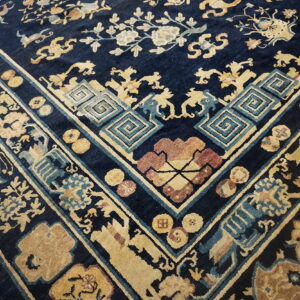 Ornate traditional rug corner featuring navy blue, beige, light blue, and maroon patterns on a wood floor.
