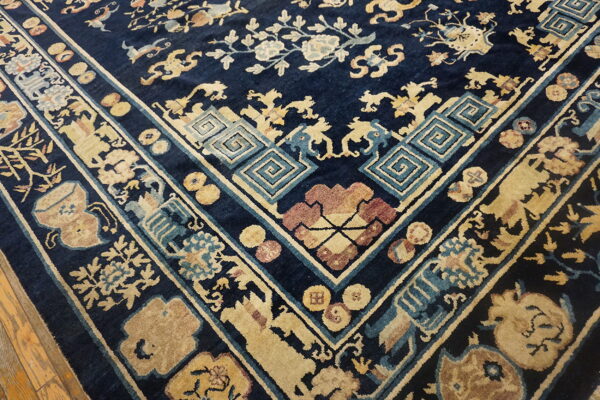 Ornate traditional rug corner featuring navy blue, beige, light blue, and maroon patterns on a wood floor.