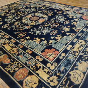 Ornate navy rug with gold and coral designs lies on distressed natural wood plank flooring.