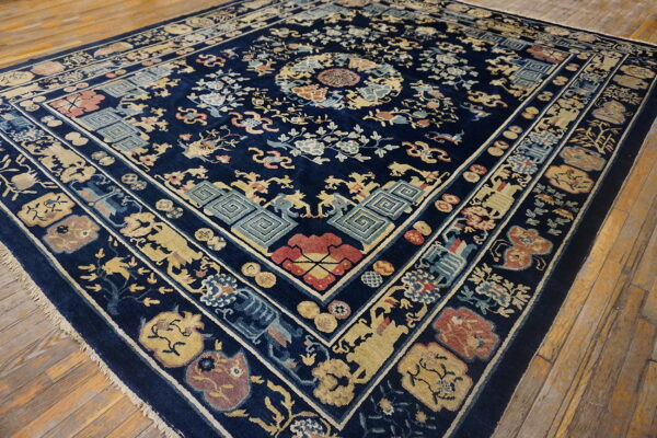 Navy blue area rug with detailed traditional motifs in gold, red, and teal on distressed wood floors.