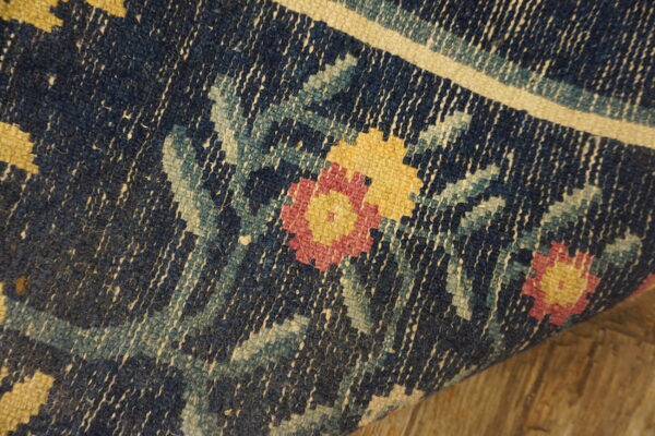 Close-up of a navy low-pile rug showing a pink and yellow floral pattern and a visible woven texture.
