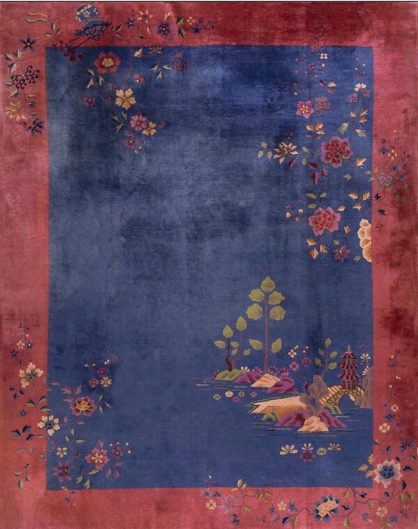 Blue rug with a wide rose-colored border, featuring floral sprays and a detailed landscape design.