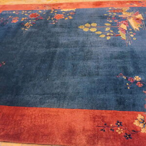 Dark blue rug with scattered colorful florals framed by a thick, rust-red border on wood floor.