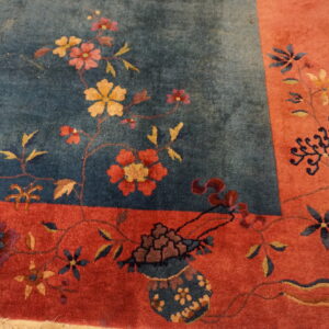 High-pile rug featuring a blue floral field and wide reddish-orange border on distressed wood flooring.