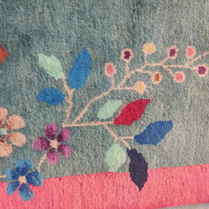 Textured teal rug detail displaying a multicolored floral vine pattern against a bright pink border strip.