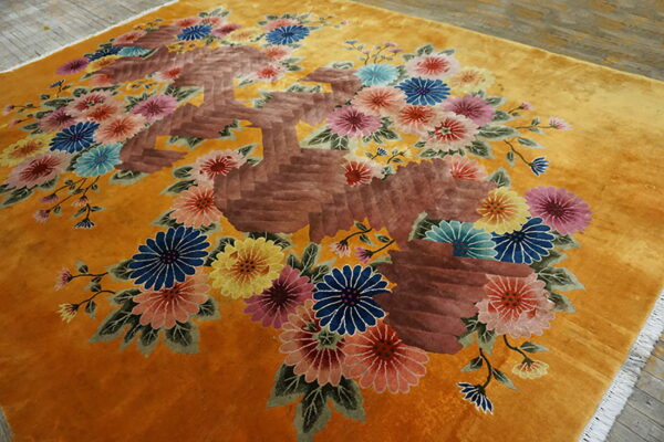 Gold high-pile rug with dense multicolored floral designs and textured brown elements on a wood floor.