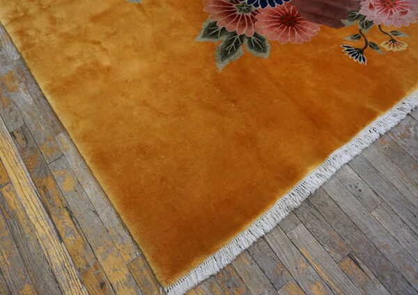 Plush golden-orange rug with pink and blue floral detail on distressed gray wood floor.