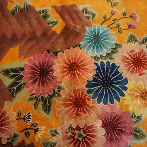 A plush, gold rug detail featuring multi-colored flowers and a bold, textured reddish-brown geometric shape.