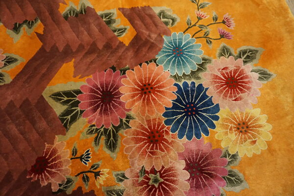 A plush, gold rug detail featuring multi-colored flowers and a bold, textured reddish-brown geometric shape.