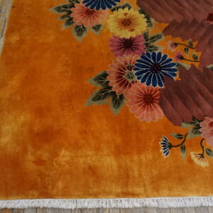 Vibrant orange rug with multicolored florals and brown abstract shapes sits on worn wood flooring.