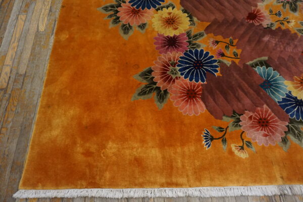 Vibrant orange rug with multicolored florals and brown abstract shapes sits on worn wood flooring.
