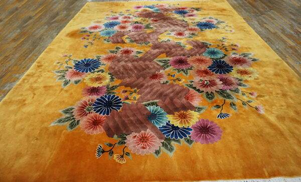 Mustard yellow rug featuring a central brown vine with multicolored floral sprays on a plank wood floor.