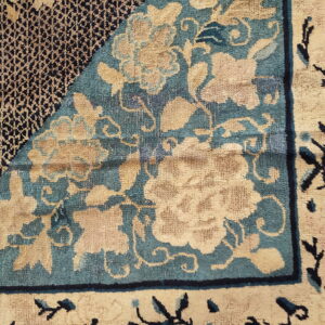 Detail of a patterned rug showing tan floral designs on a teal ground next to a dark blue geometric field.