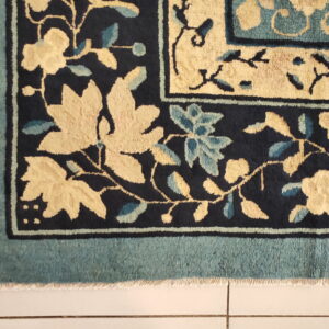 Navy rug corner shows pale yellow and light blue floral motifs within a structured teal border design.