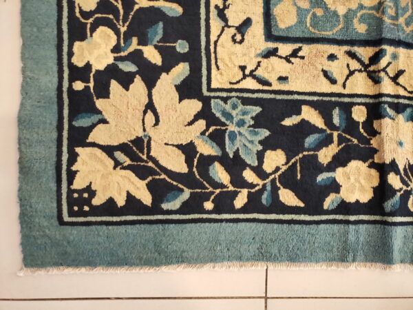 Navy rug corner shows pale yellow and light blue floral motifs within a structured teal border design.