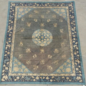 Ornate floral rug with a central medallion, dark field, and multi-layered blue and beige borders on concrete.