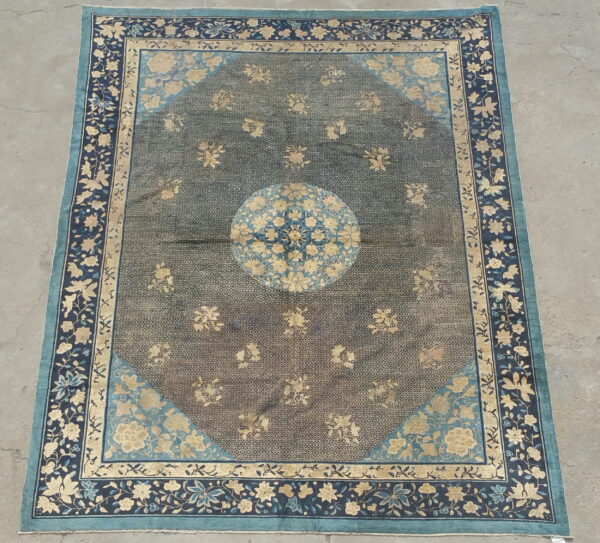Ornate floral rug with a central medallion, dark field, and multi-layered blue and beige borders on concrete.