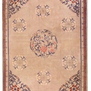 Plush tan rug featuring a central floral pattern in blue, coral, and maroon with geometric borders.