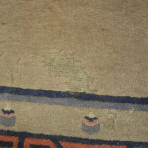 Worn tan rug texture exposing the woven foundation with blue and rust colored border patterns.