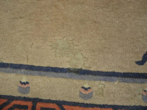 Worn tan rug texture exposing the woven foundation with blue and rust colored border patterns.