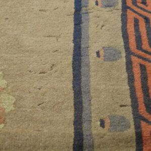 Detail of a tan rug with striped geometric patterns in dark blue and coral hues.