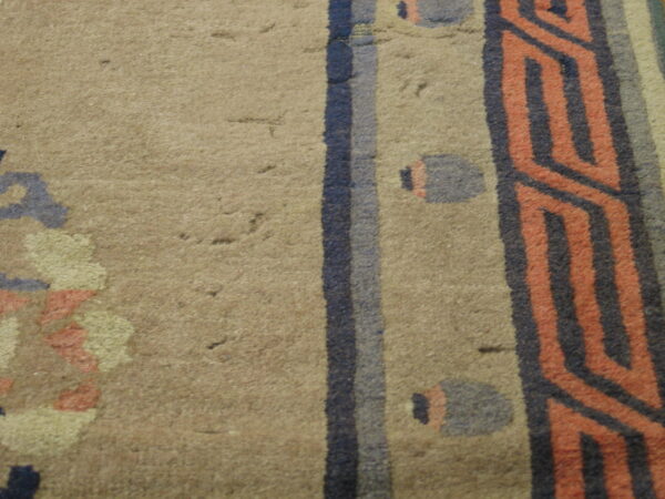 Detail of a tan rug with striped geometric patterns in dark blue and coral hues.