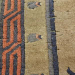 A tan rug detail featuring a medium pile and a border pattern of zigzag coral and dark blue stripes.