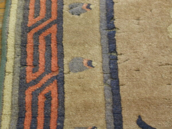 A tan rug detail featuring a medium pile and a border pattern of zigzag coral and dark blue stripes.