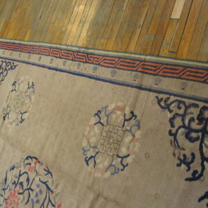Taupe rug with blue and coral floral roundels and a geometric border rests on polished wood floors.