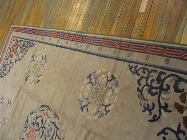 Taupe rug with blue and coral floral roundels and a geometric border rests on polished wood floors.