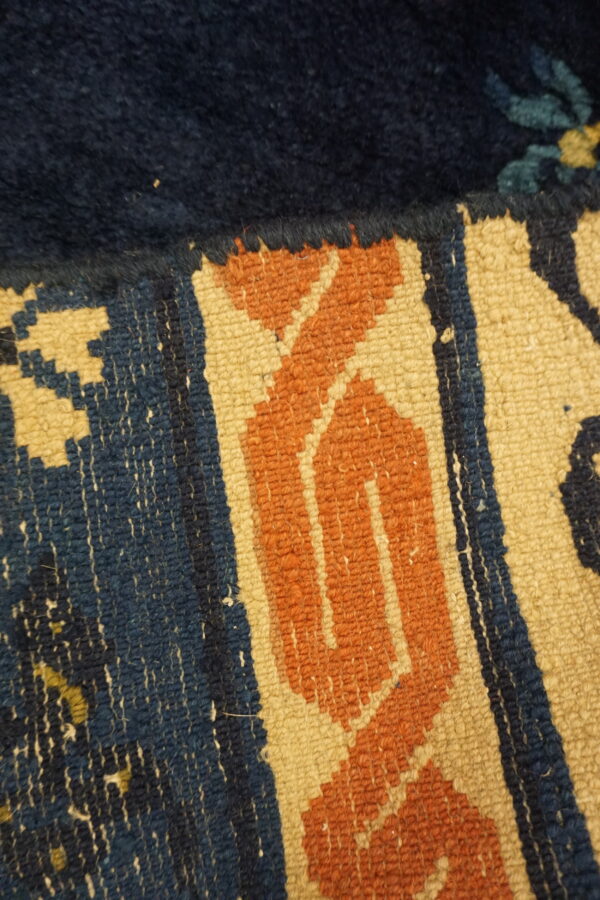 Detail shot of a rug featuring high indigo pile next to a rust and tan flatweave geometric border.
