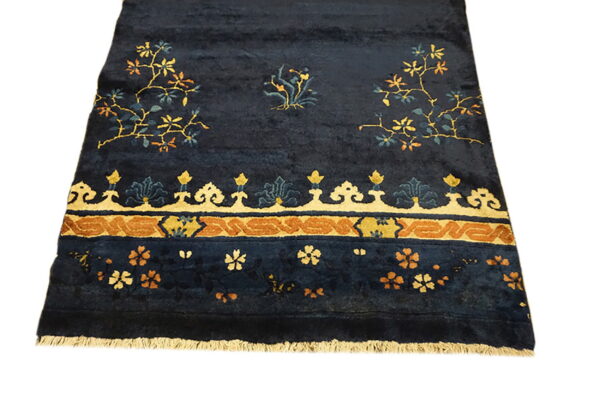 Navy blue plush rug with stylized gold and rust floral vines and an elaborate patterned border.