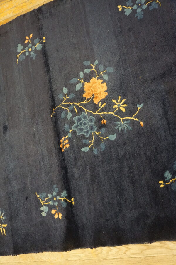 A dark blue rug with scattered gold and teal floral motifs rests on a light wood floor.