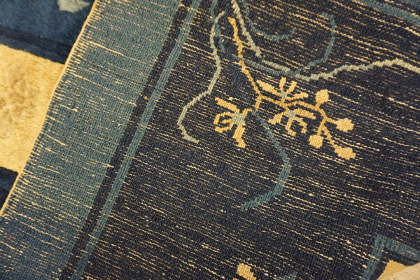 Detail of a low-pile dark blue rug showing tan geometric patterns and teal lines, adjacent to a tan high-pile rug.