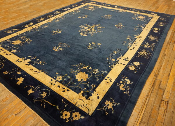 Large blue rug featuring traditional gold and navy floral patterns on a worn wooden plank floor.